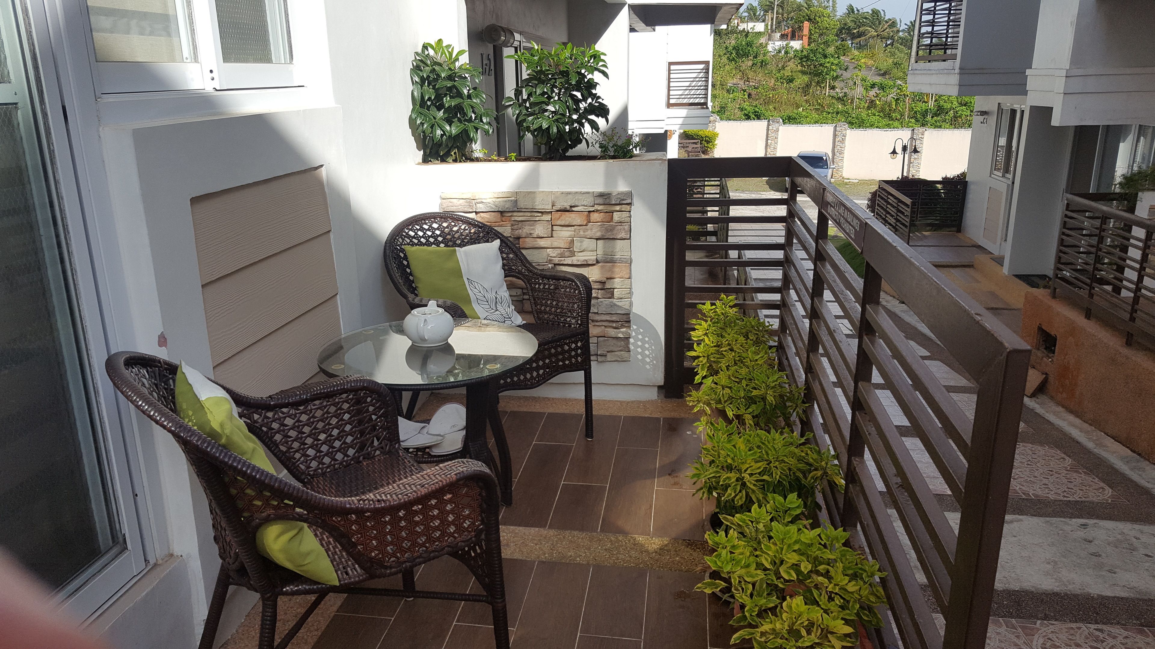 Un patio con sillas de mimbre, una mesa de vidrio y una tetera blanca.