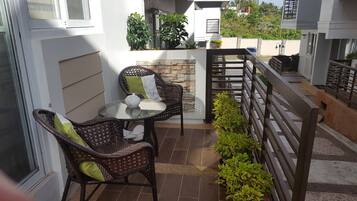 Un patio con sillas de mimbre, una mesa de vidrio y una tetera blanca.
