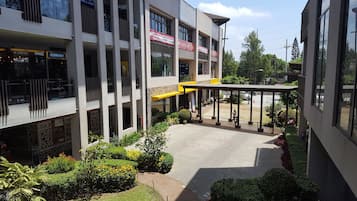 Un edificio moderno de varios pisos, un paseo techado y un patio ajardinado con diversas plantas.