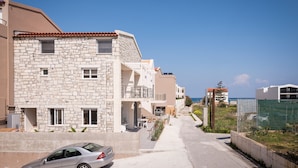 A row of stone buildings with balconies, a car parked in front, and a clear view of the sea in the background. - Athina Apartments (Platanias)
