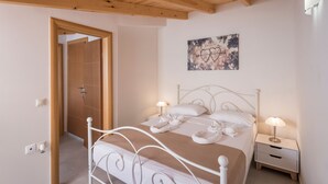 A bedroom with a wooden ceiling, a bed with white bedding, two bedside tables with lamps, and a door leading to another room. - Athina Apartments (Platanias)