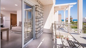 A modern room with a glass door leading to a balcony, a bed, a small table, and a view of the sea. - Athina Apartments (Platanias)