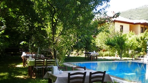 An outdoor dining area with tables and chairs, a swimming pool, and a building in the background. - Defne Pansiyon (Marmaris)