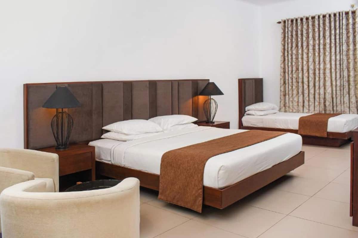 Habitación de hotel con una cama grande, dos mesitas de noche, una silla y un ventanal con cortinas.