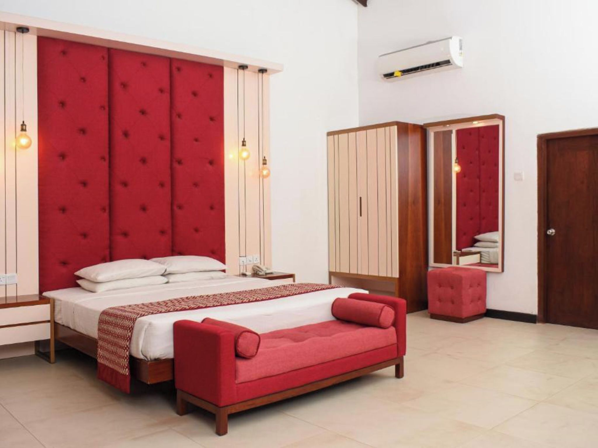 A bedroom with a large bed, a red sofa, a wardrobe, and a mirror.
