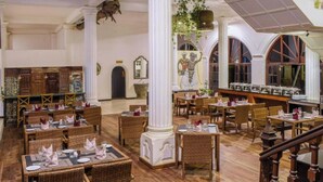 Un vaste espace dédié à la salle à manger, avec des chaises et des tables en osier, des colonnes blanches et un escalier.