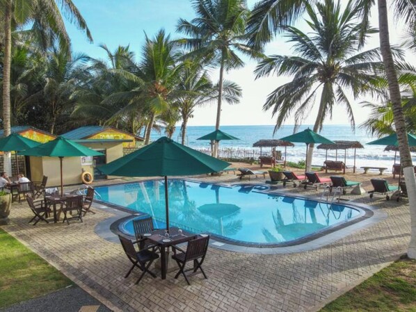 Ein Poolbereich mit Liegestühlen und Sonnenschirmen, umgeben von Palmen und Blick auf das Meer.