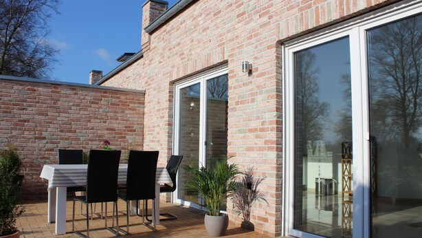 A patio with a table and chairs, a potted plant, and a brick wall. - 100 sqm large, central and quiet holiday home in Rhauderfehn! (Rhauderfehn)