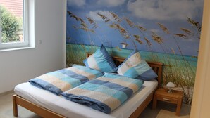 A bedroom with a bed, a nightstand, a lamp, and a mural of a beach scene. - 100 sqm large, central and quiet holiday home in Rhauderfehn! (Rhauderfehn)