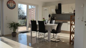 A modern kitchen with white cabinets, a black range hood, and a dining area with a striped tablecloth and black chairs. - 100 sqm large, central and quiet holiday home in Rhauderfehn! (Rhauderfehn)