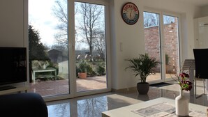 A modern living room with a large sliding glass door leading to a patio area. - 100 sqm large, central and quiet holiday home in Rhauderfehn! (Rhauderfehn)