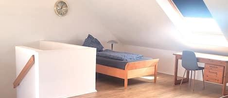 A loft bedroom with wooden beams, a skylight, a bed, a desk, and a chair.