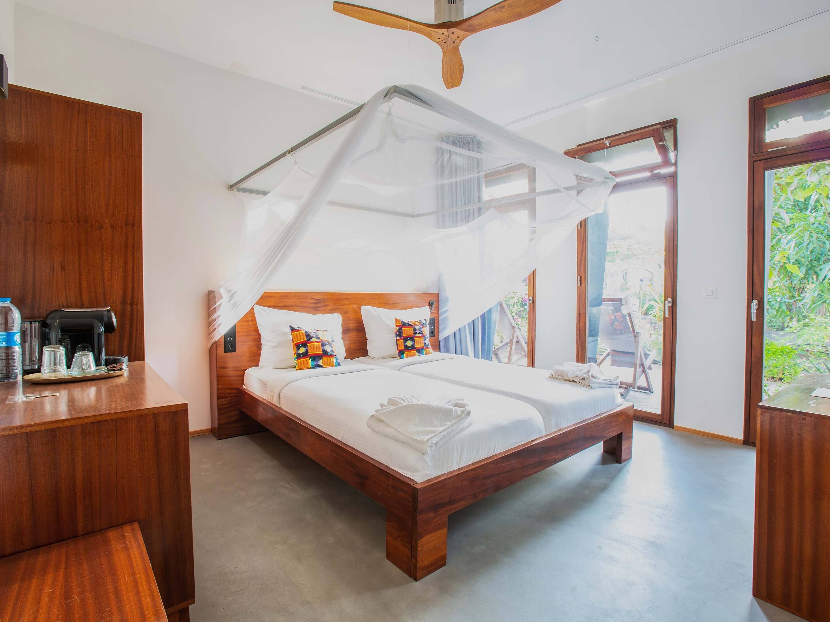 Una habitación con una cama de madera, una mesita de noche de madera, una cafetera y una ventana con vistas a la vegetación.