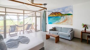 Un soggiorno moderno con una grande finestra, un divano, un tavolino da caffè e un quadro raffigurante una spiaggia.