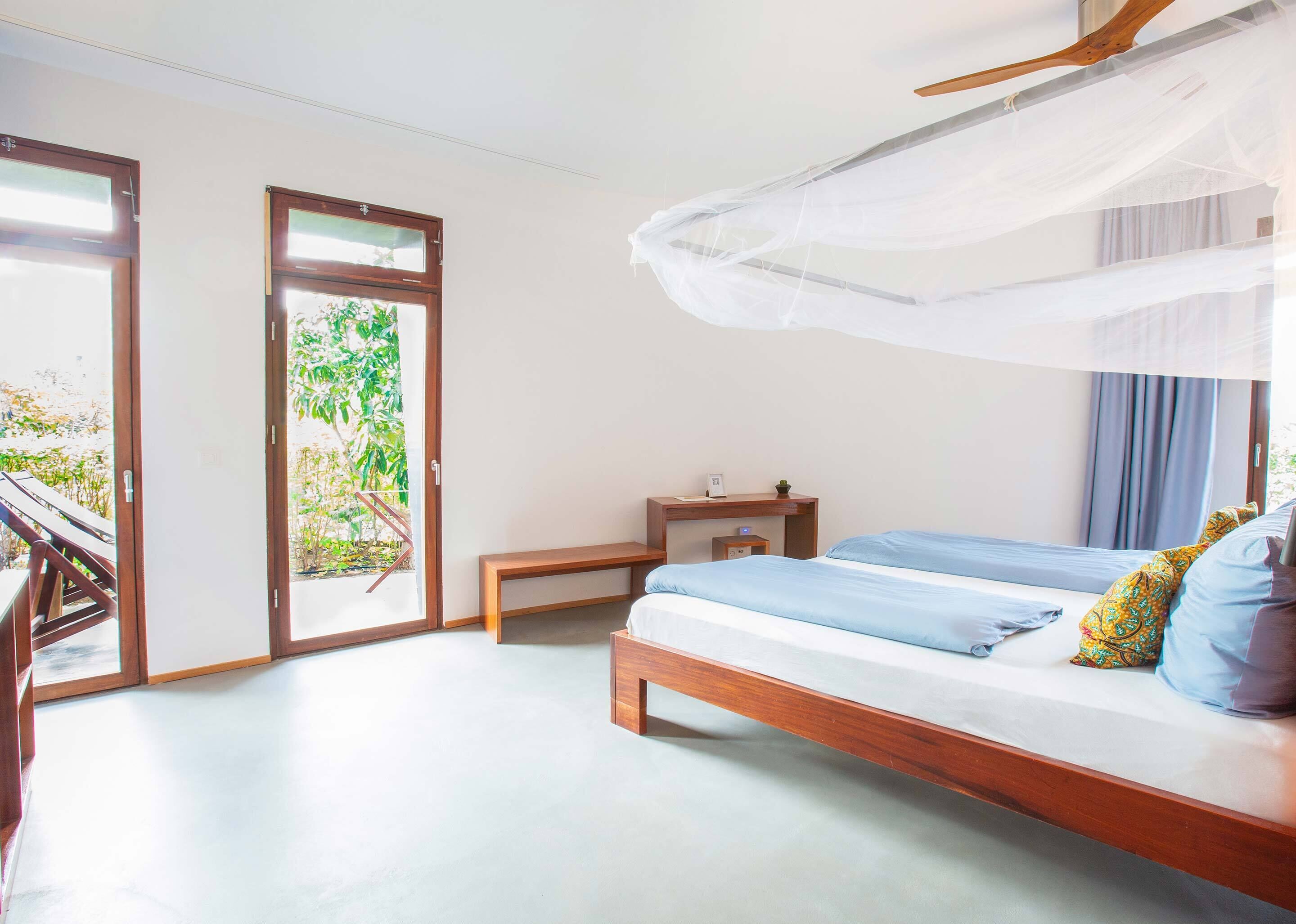 A bedroom with a bed, bedside table, and a window with a view of greenery.