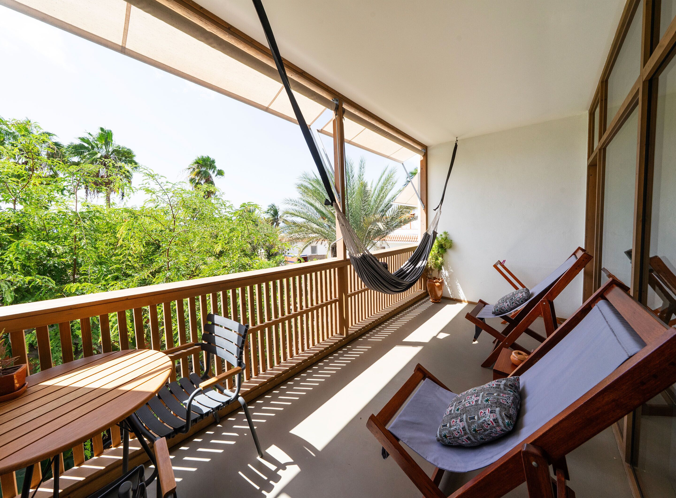 A balcony with wooden railings, a hammock, and two lounge chairs with cushions.