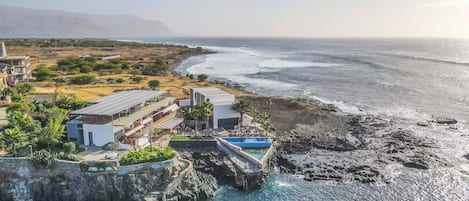 A coastal hotel with a pool, a rocky shoreline, and a view of the ocean.