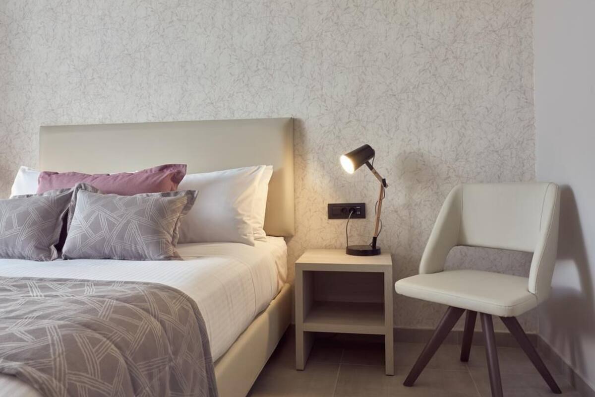 A neatly arranged bedroom with a bed, bedside lamp, and a chair.