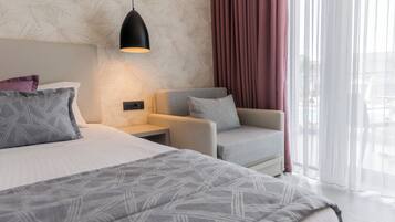 A modern hotel room with a large bed, a seating area with a chair, a nightstand, and a wall-mounted lamp.