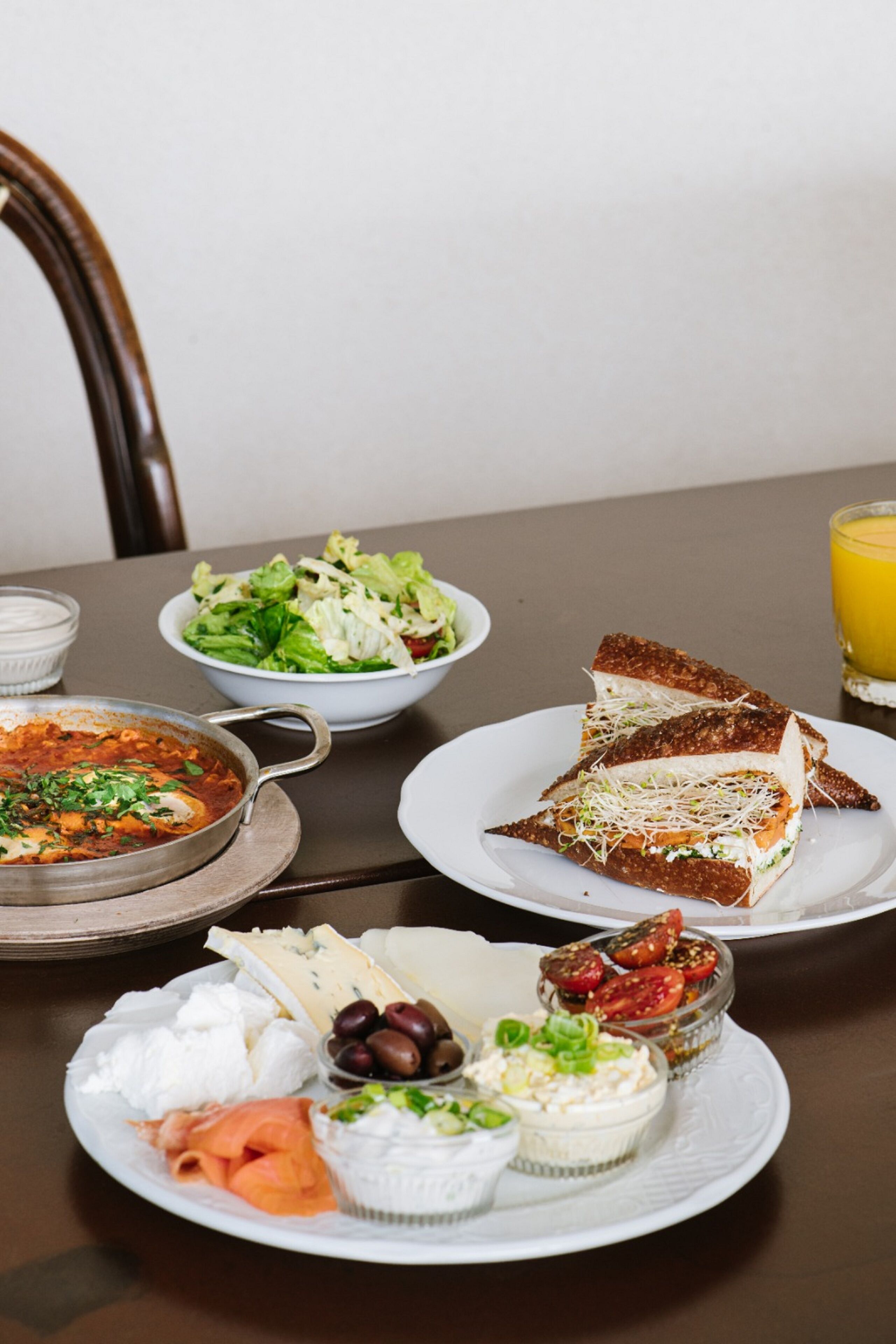 Een tafel met diverse soorten eten, waaronder een salade, belegde broodjes en een gerecht met rode saus.