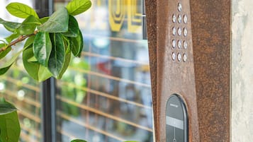 Un panneau de commande d’ascenseur rouillé, doté d’un clavier et d’un bouton, fixé à un mur avec une fenêtre en arrière-plan.