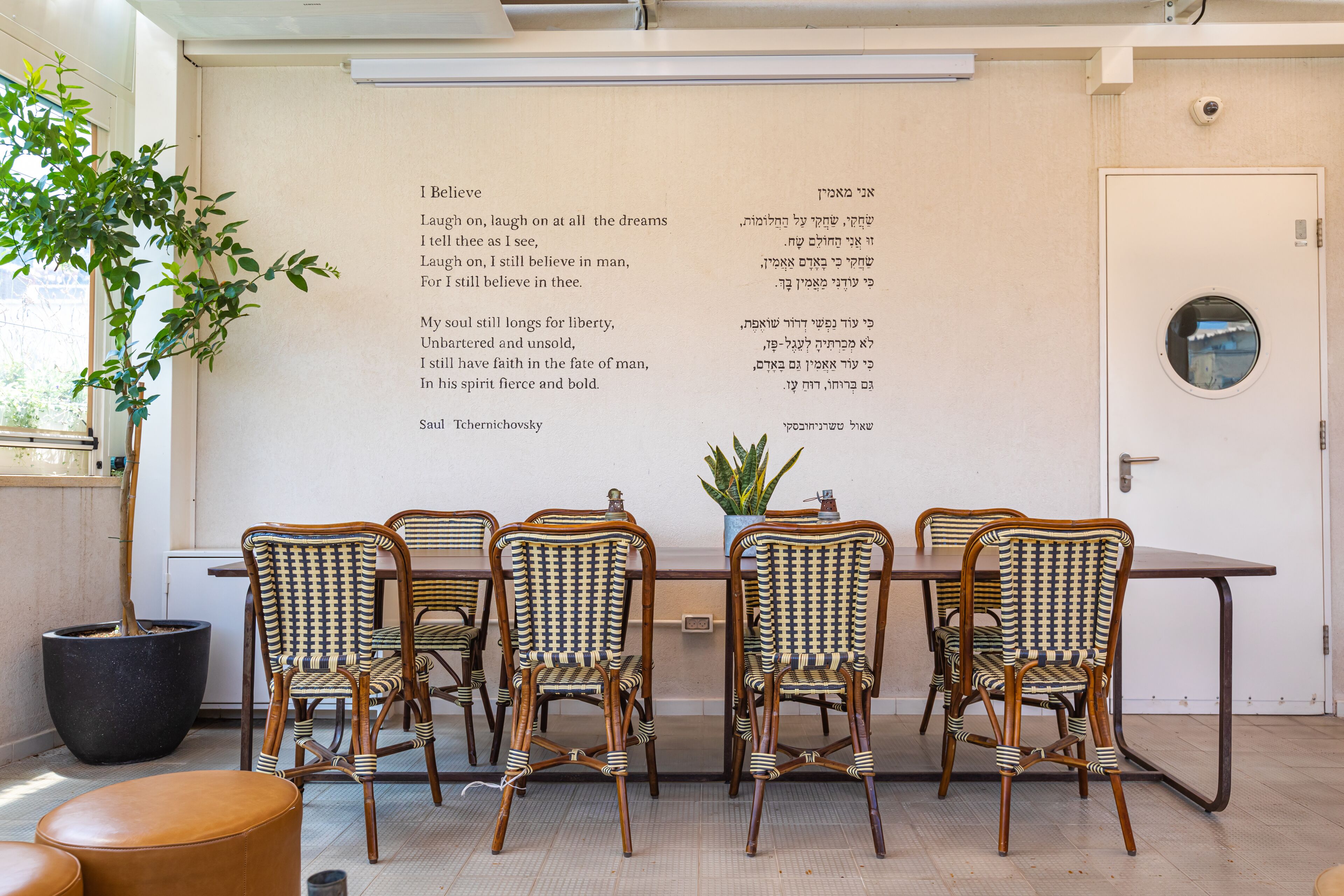 Un comedor con una mesa y cuatro sillas de mimbre, una planta en maceta y una pared con texto.