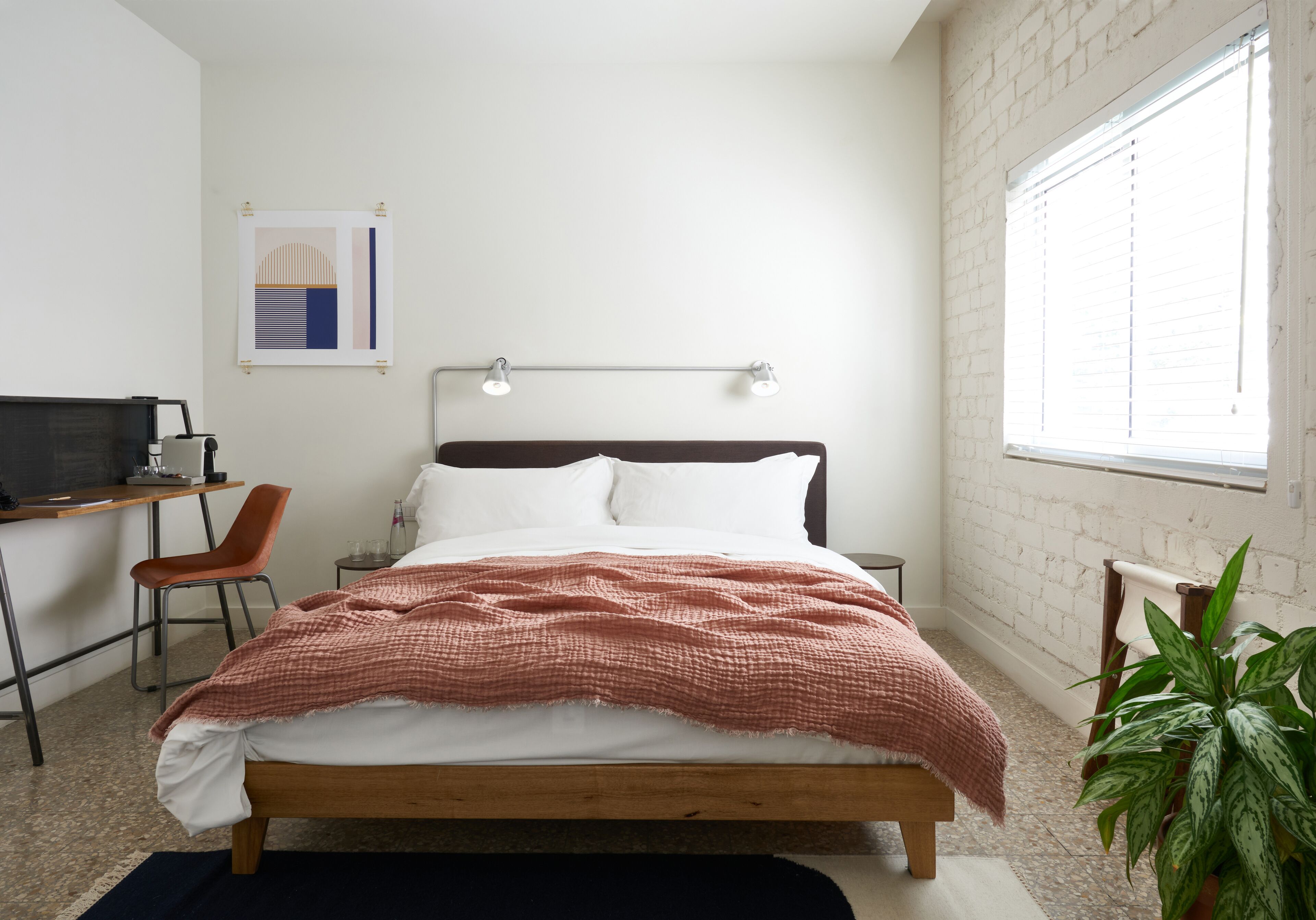 A bedroom with a bed, desk, chair, and a potted plant.