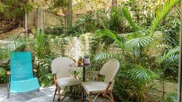 A patio with two striped chairs and a turquoise chair, surrounded by lush greenery and a stone wall.