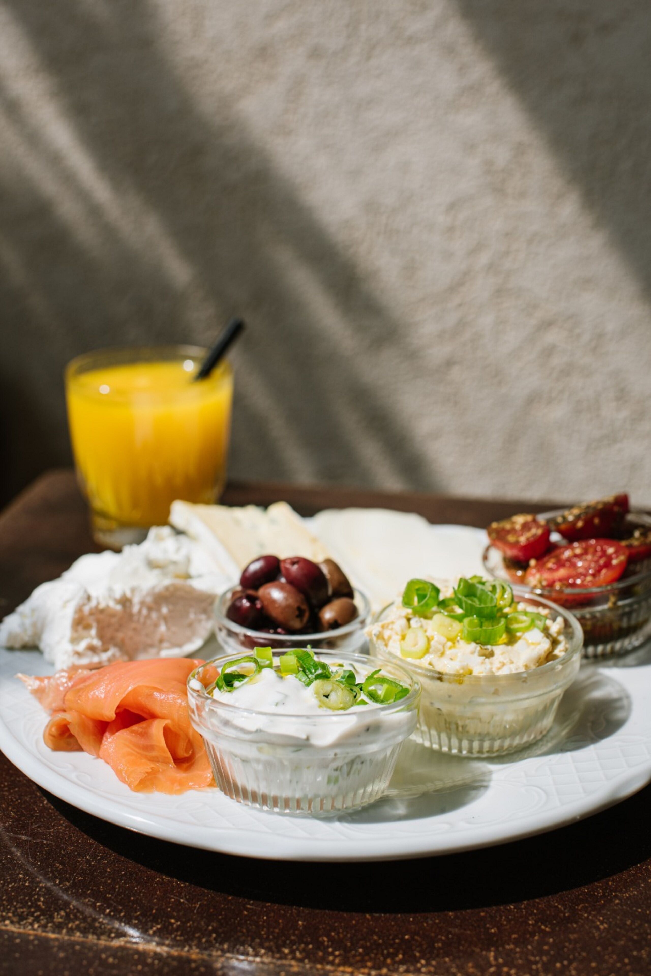 A plate with various food items including smoked salmon, cheese, olives, and a glass of orange juice.