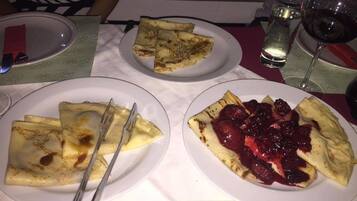 Een tafel met borden eten, waaronder pannenkoeken en een dessert met bessen.