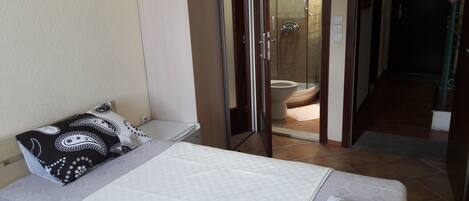Una habitación de hotel con una cama, una mesita de noche, un baño con ducha y un inodoro.