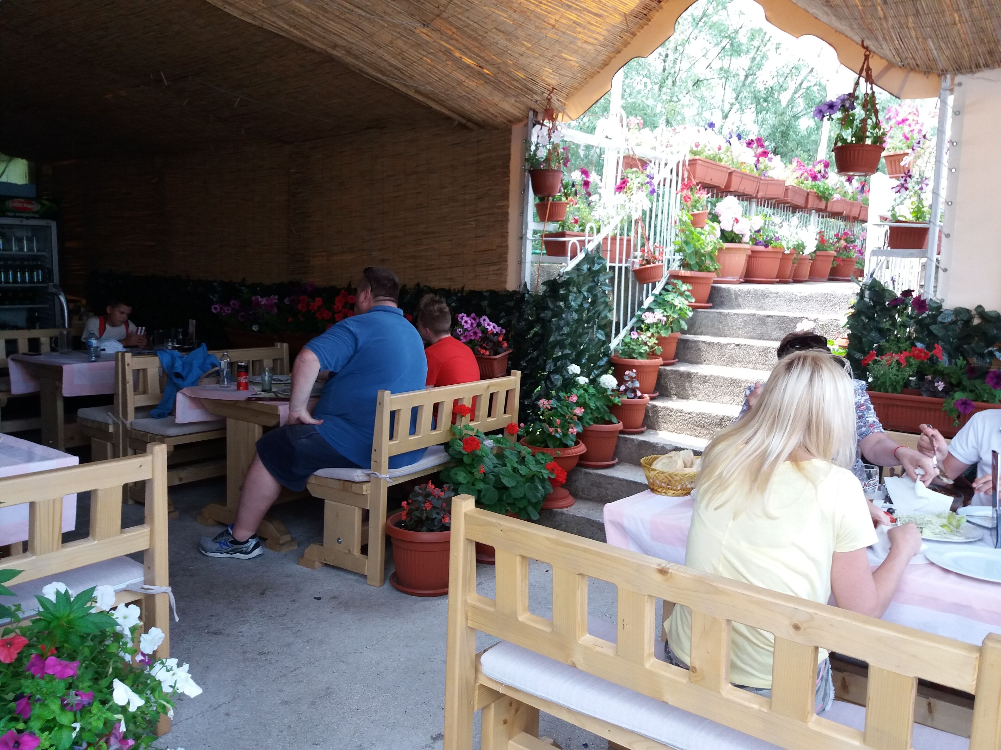 An outdoor café with wooden tables and chairs, surrounded by potted plants and flowers.
