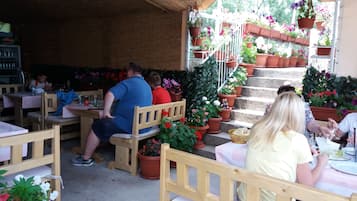 An outdoor cafรฉ with wooden tables and chairs, surrounded by potted plants and flowers.