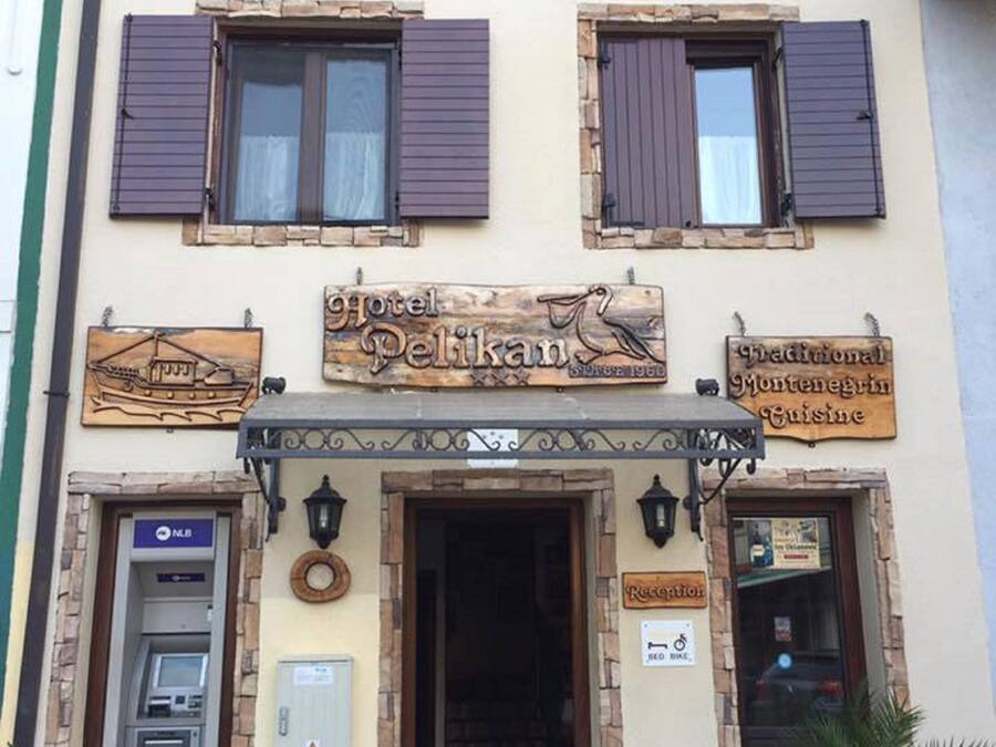 A hotel named "Hotel Pelikan" with a traditional facade, a reception desk, and a sign indicating Montenegrin cuisine.