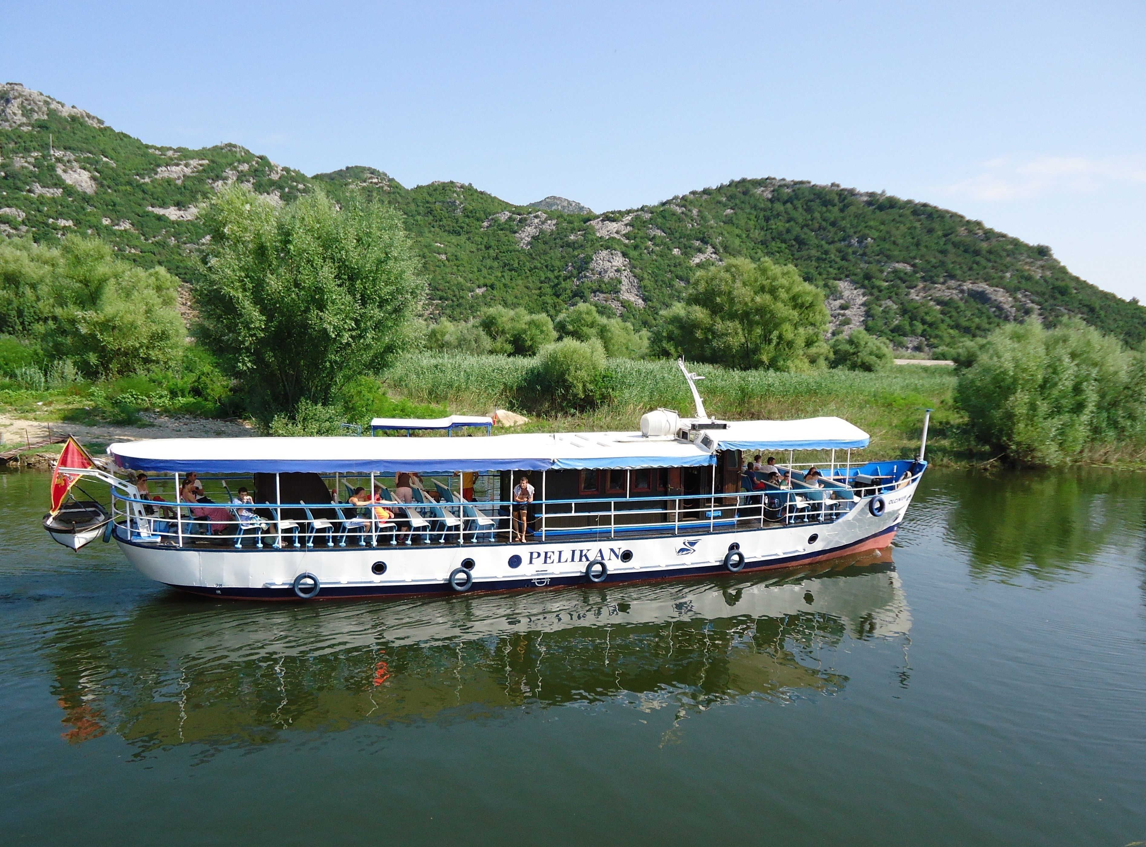 A riverboat with passengers, surrounded by lush greenery and hills.