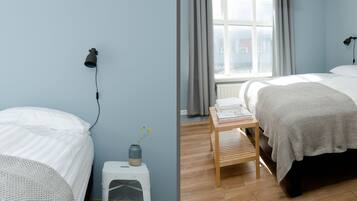 Un dormitorio con dos camas, una mesita de noche de madera, una ventana con cortinas y una lámpara fijada a la pared.