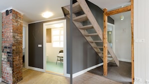 Una habitación con chimenea de ladrillo, escalera de madera y vista al baño.