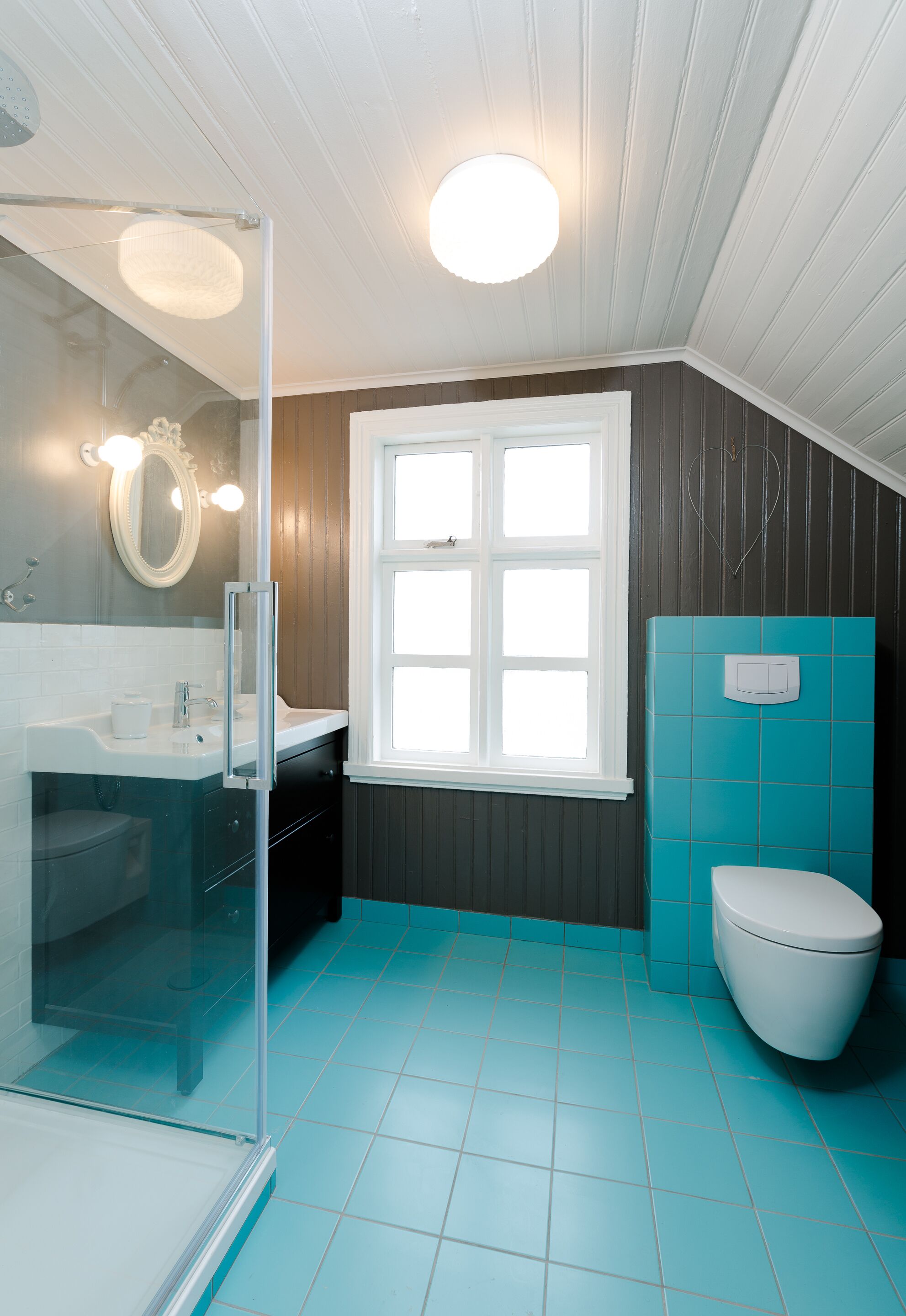 A bathroom with a glass shower enclosure, a white toilet, and a window with white frames.