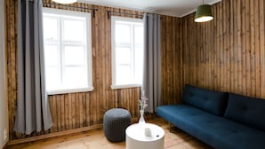 Una habitación con paredes de paneles de madera, un sofá azul, una mesa redonda blanca y cortinas grises.
