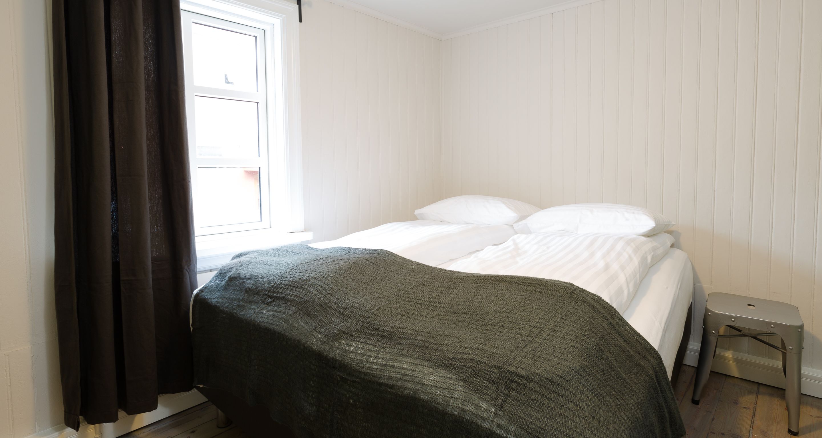 Un dormitorio con cama, ventana con cortinas y una mesita.