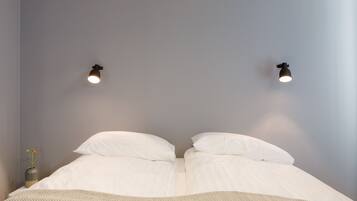 Un dormitorio con una cama, dos luces fijadas a la pared y un pequeño florero con flores en la mesita de noche.