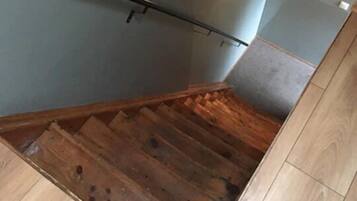 Un escalier en bois avec une rampe, un panneau de signalisation verte indiquant la sortie et un luminaire au-dessus.