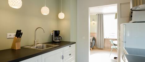 Een keuken met een zwart aanrecht, witte kasten, een koffiezetapparaat en hangende hanglampen.