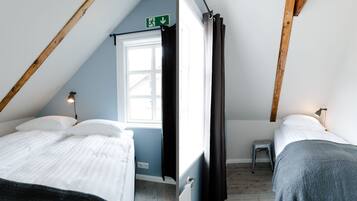 A small, cozy room with two beds, a window, and a wooden ceiling.