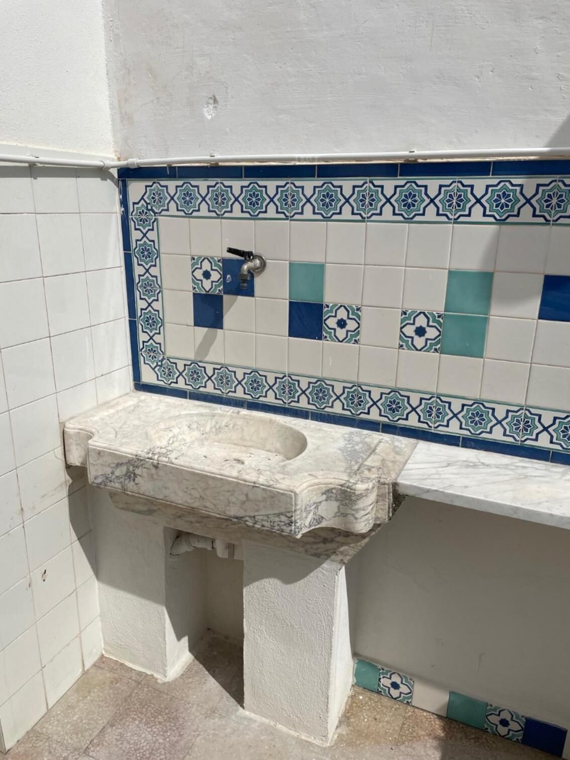 Un baño con lavamanos de mármol, salpicadero de azulejos con diseños azules y blancos, y pared blanca.