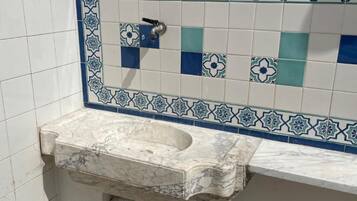 Un baño con lavamanos de mármol, salpicadero de azulejos con diseños azules y blancos, y pared blanca.