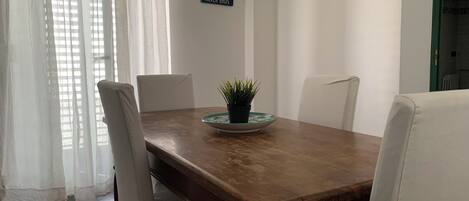 Ein Essbereich mit einem Holztisch, weißen Stühlen, einer Kü Pflanze und einem 'WELCOME'-Schild an der Wand.