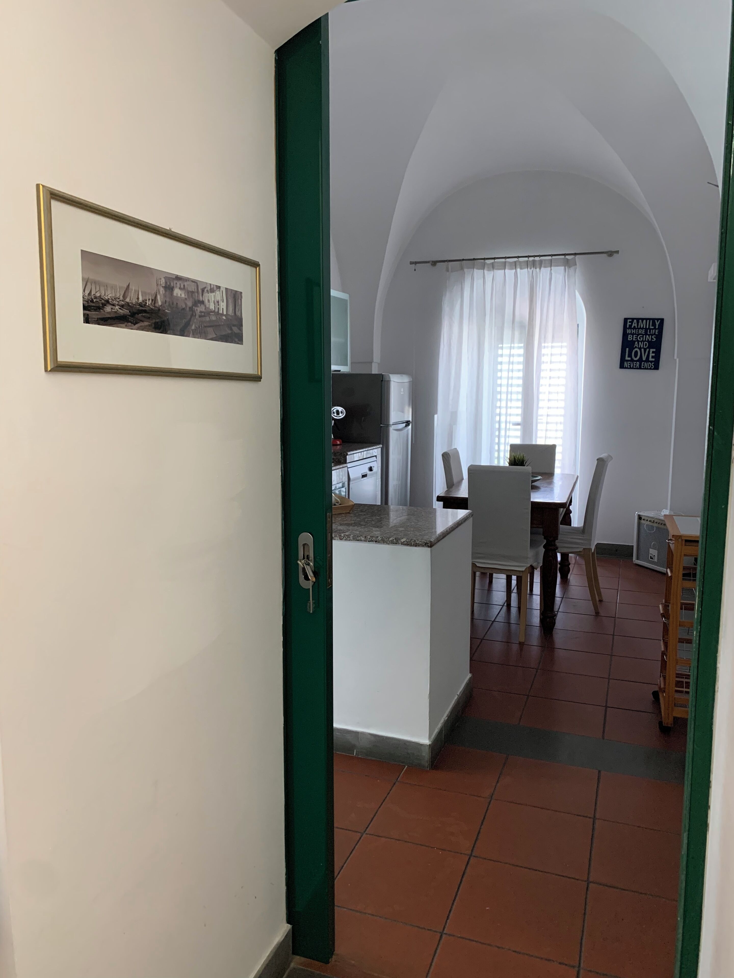 Una cocina con zona de comedor, una puerta verde, un cuadro enmarcado y un letrero en la pared.