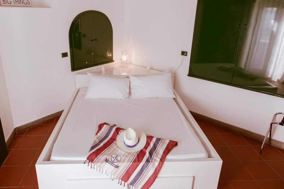 A neatly made bed with white linens, a striped throw blanket, and a white hat on the bed.