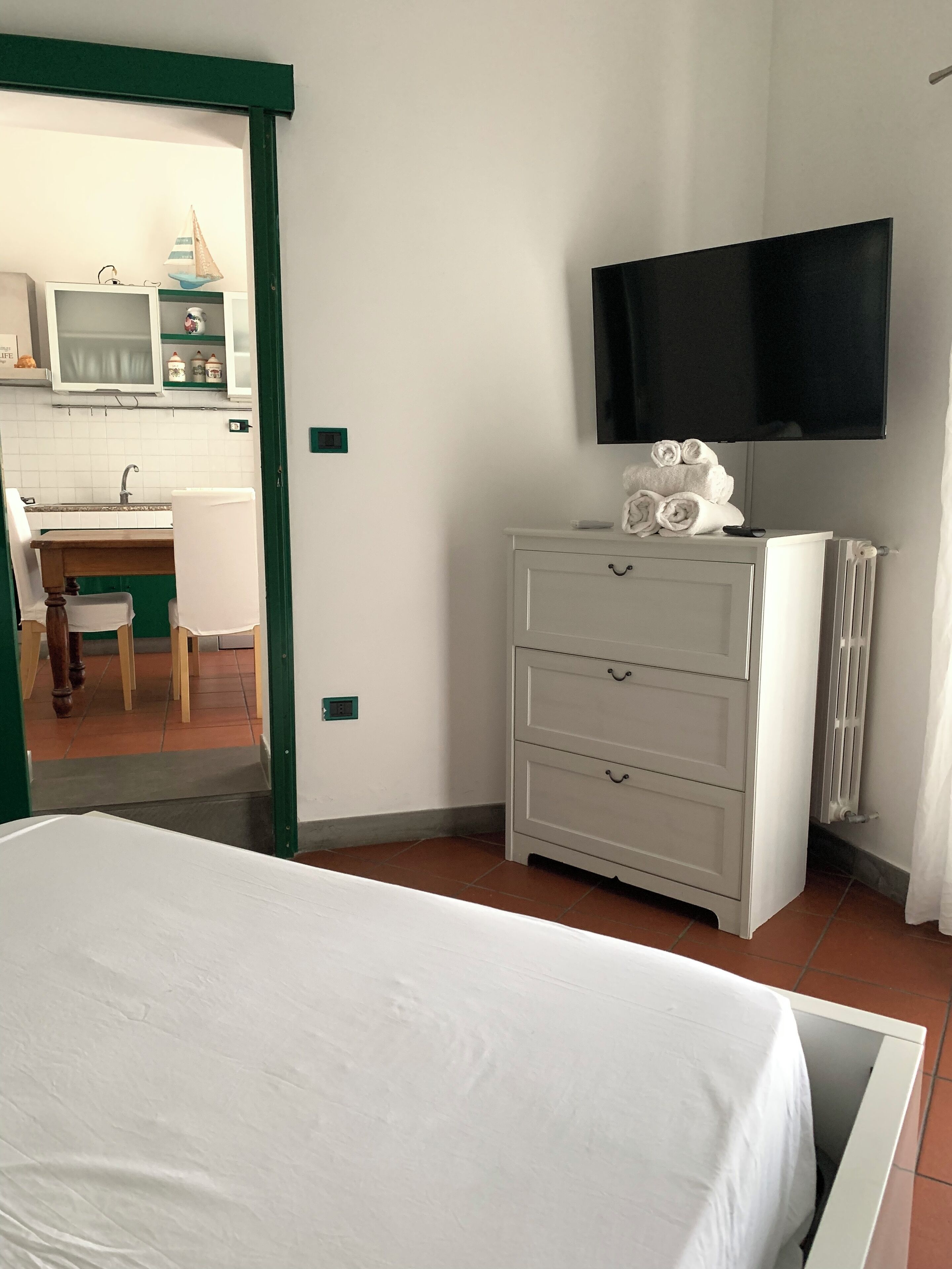 Un dormitorio con cama, cómoda, televisor montado en la pared y vistas a una zona de cocina.